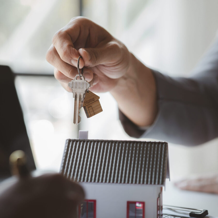 A home rental company employee is handing the house keys to a customer who has agreed to sign a rental contract, explaining the details and terms of the rental. Home and real estate rental ideas.